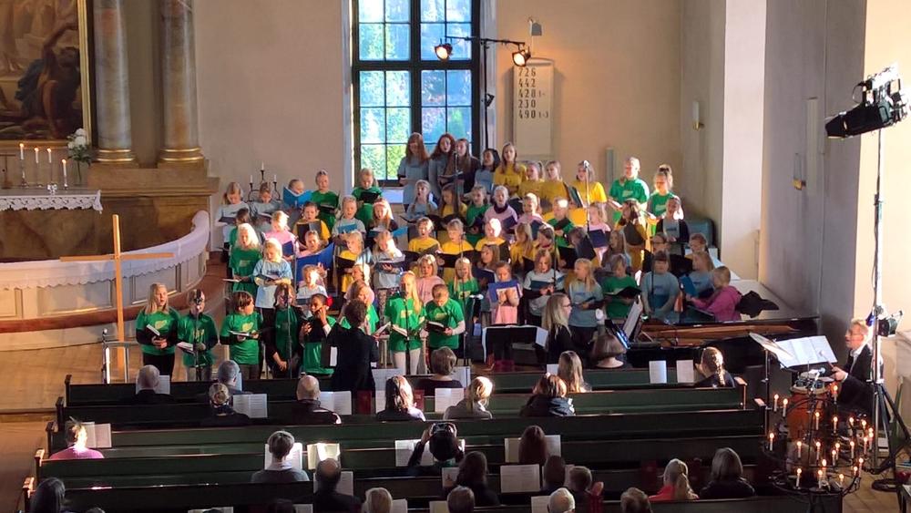 Noin 60 lapsikuorolaista laulamassa värikkäissä paidoissaan Uskelan kirkossa