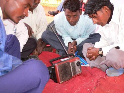 Neljä intialaista miestä istuu maassa ja kuuntelee radiota