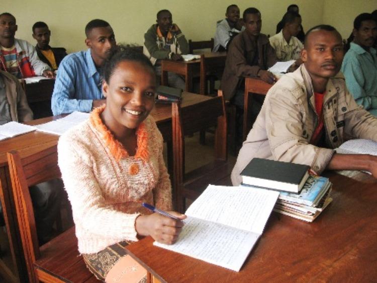 Nuori nainen ja miehiä istumassa etiopialaisessa raamattukoulussa.
