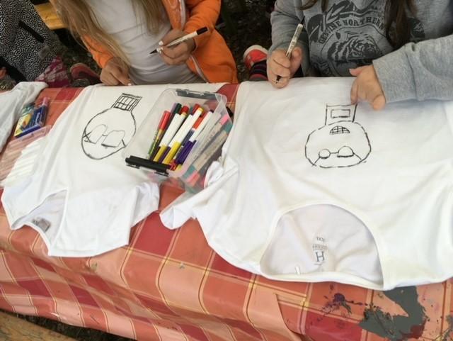 Kaksi lasta piirtää kuvia T-paitoihin.