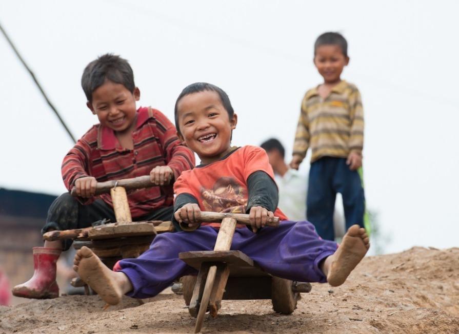 Laoslaiset pikkupojat laskevat mäkeä puisilla mäkiautoillaan.