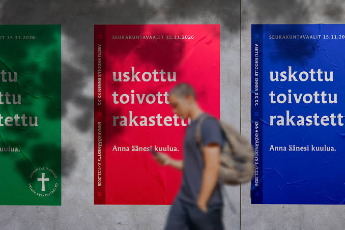Henkilö reppu selässä, kännykkä kädessä, takana vaalijulisteet seinällä.